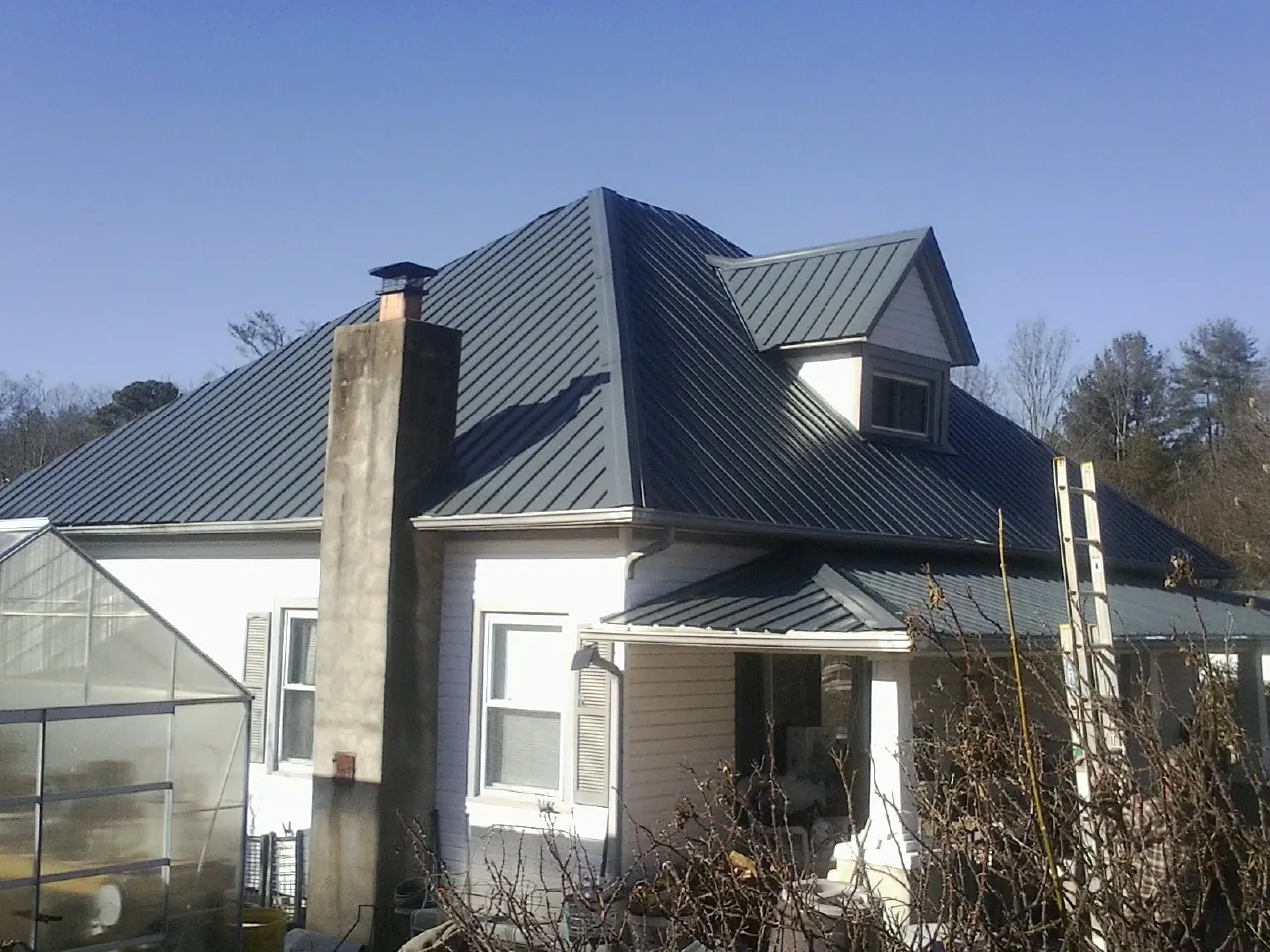 Dark blue standing seam metal roof on a white farmhouse with dormer — Slate & Tile Roof Repair by Roofing Brothers in Truxton