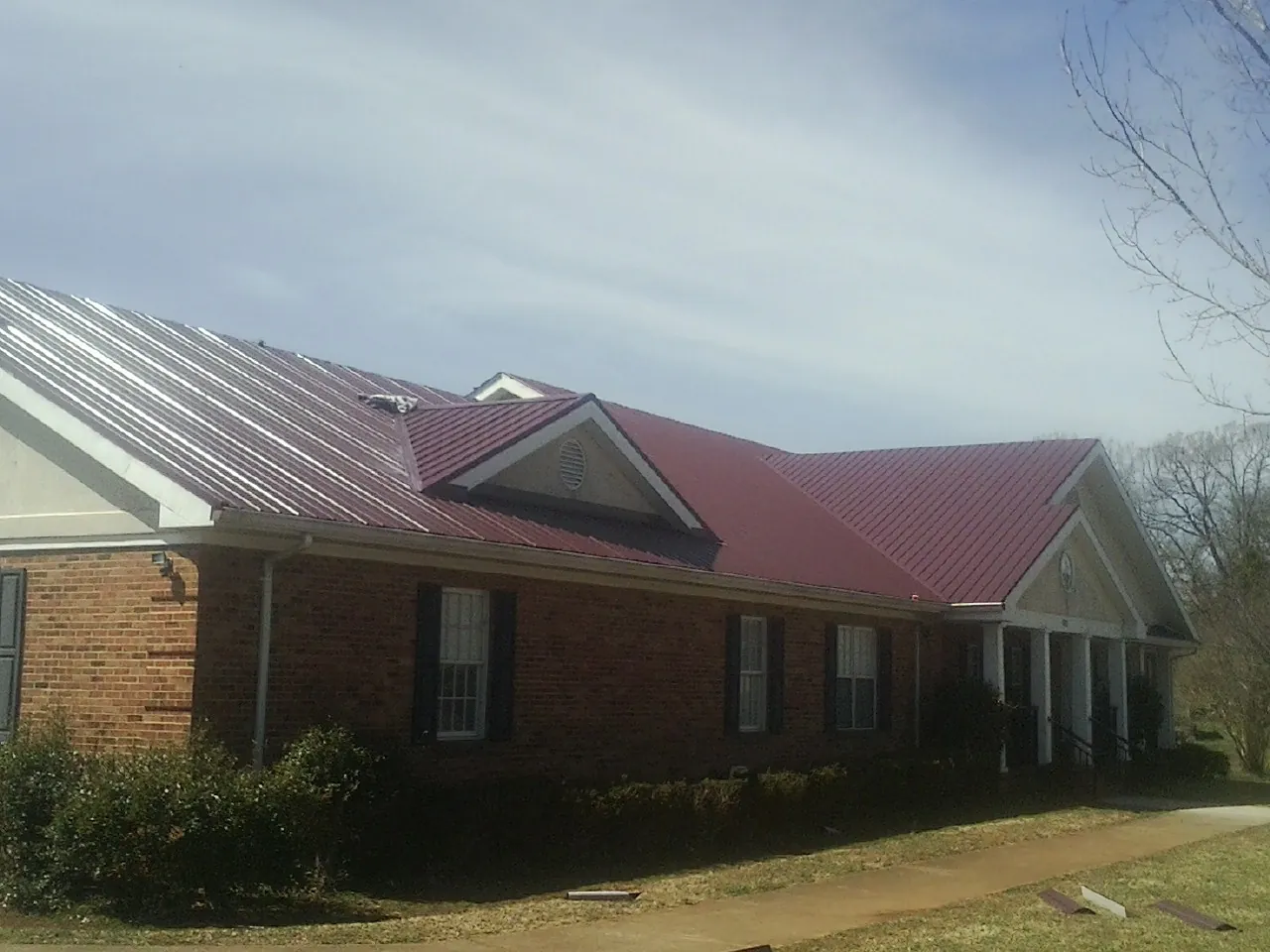 Red metal roof with gabled entries on a long brick building, from a Hail Damage Roof Repair job in Truxton