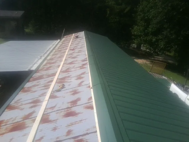 Old rusted panels beside newly installed green metal roofing — Wind Damage Roof Repair by Roofing Brothers in Truxton
