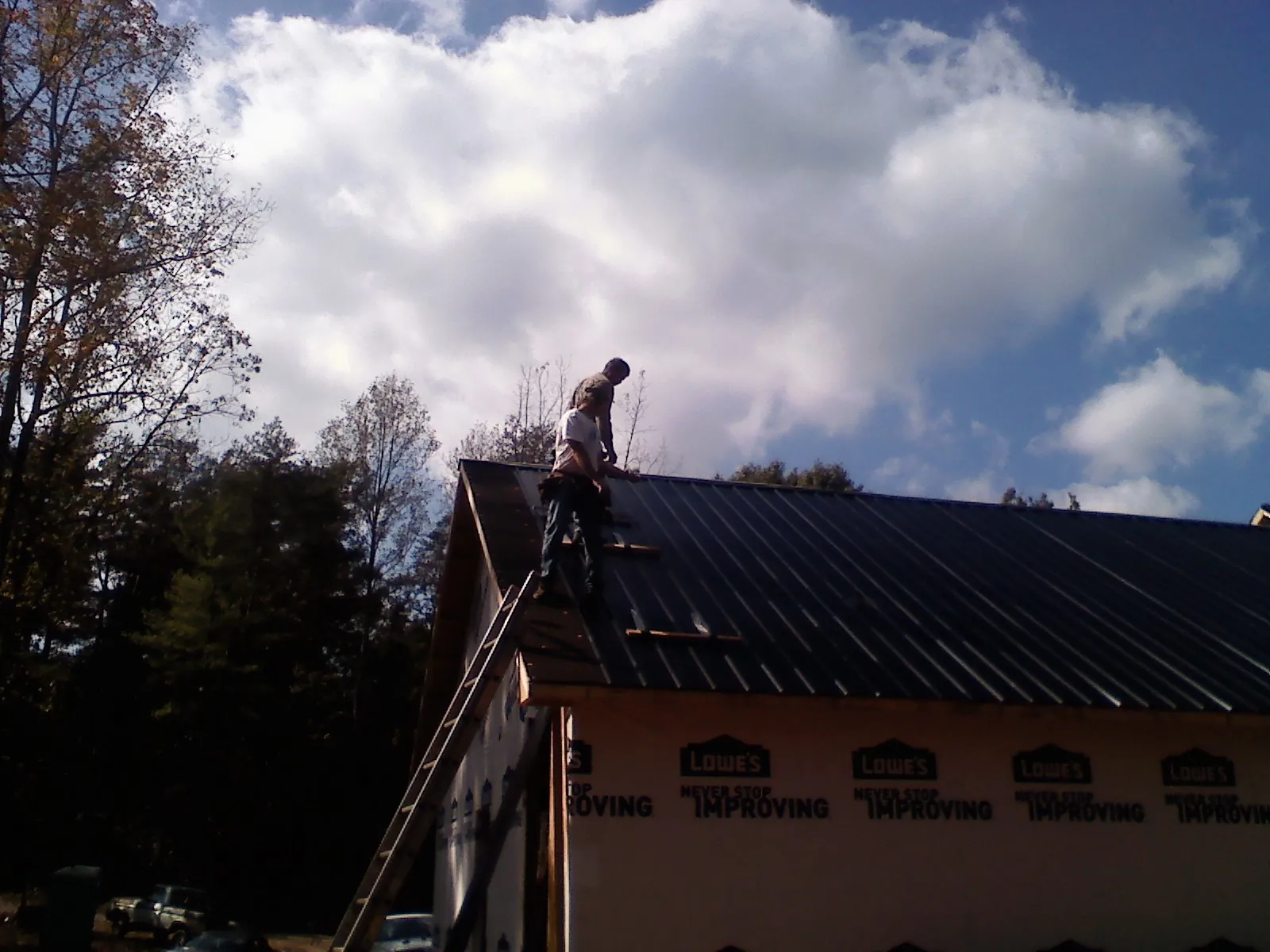 Roofer fastening dark metal panels high against a cloudy sky, from a Roof Inspection job in Truxton