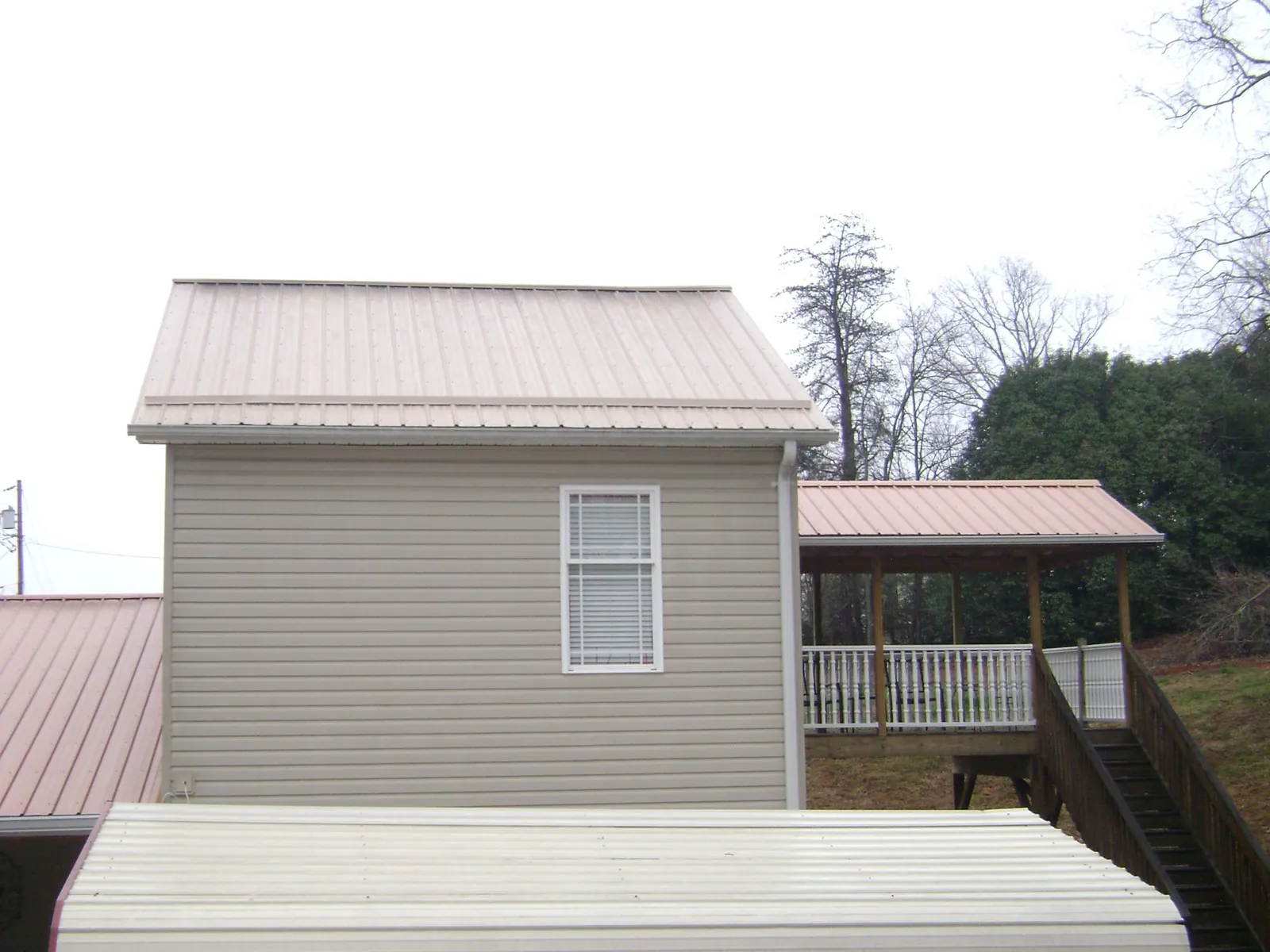Tan metal roofs on a two story addition and attached porch, from a Roof Replacement job in Truxton